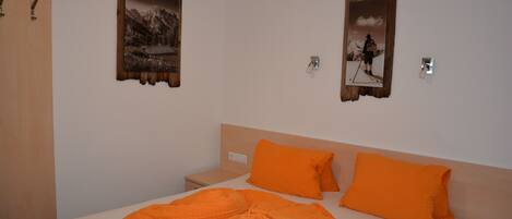 A hotel room with a bed, two pillows, a nightstand, and two wall-mounted pictures.