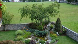 A garden with a pond, various plants, and a stone wall. - Apartment with beautiful terrace to relax (Kapfing)