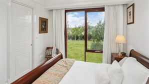 Habitación de hotel con cama, mesita de noche, silla, ventana y vista a zonas verdes, además de una puerta.