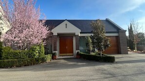 Una casa moderna de dos pisos con puerta principal de madera, garaje y un jardín bien cuidado con árboles en flor.