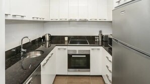 Una cocina compacta con armarios blancos, un lavamanos de acero inoxidable, horno integrado y refrigerador.