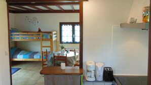 Une cuisine compacte avec un petit îlot central, un coin repas avec une table et des chaises, et un lit superposé à l’arrière-plan.