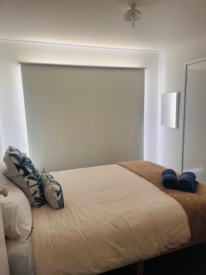 A bedroom with a bed, pillows, a blanket, and a mirror on the wall. - Cosy Family Home 500 metres from Red Rock Beach (Cowes)