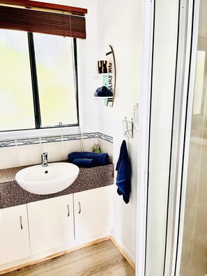 A bathroom with a white sink, a window with blinds, a towel rack, and a surfboard decoration. - Cosy Family Home 500 metres from Red Rock Beach (Cowes)