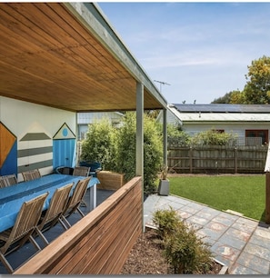 Relax on the patio with a long bench and dining table, surrounded by a garden and a well-maintained lawn.