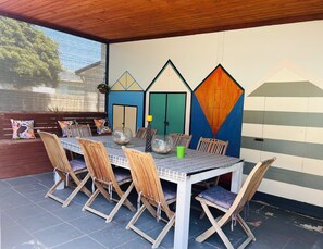 An outdoor dining area with a table set for six, surrounded by wooden chairs with cushioned seats. - Cosy Family Home 500 metres from Red Rock Beach (Cowes)