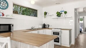 A modern kitchen with white cabinetry, a wooden island, and a large window. - Cosy Family Home 500 metres from Red Rock Beach (Cowes)