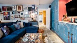 Un salon avec un canapé bleu, une table basse sur laquelle sont posés des magazines et un mur décoré de tableaux encadrés.