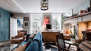 Un salon chaleureux avec un canapé bleu, un fauteuil en bois et un coin repas comprenant une table et des chaises.