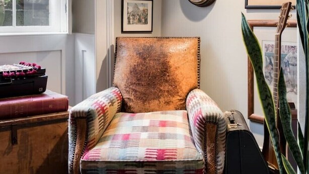 Un coin lecture confortable avec un fauteuil en cuir, une horloge murale, des photos encadrées et une plante en pot.