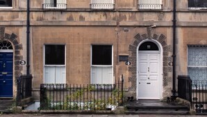 Un immeuble à plusieurs étages doté d’une façade symétrique, avec des fenêtres régulièrement espacées, une entrée centrale surmontée d’une arche décorative et une porte bleue.