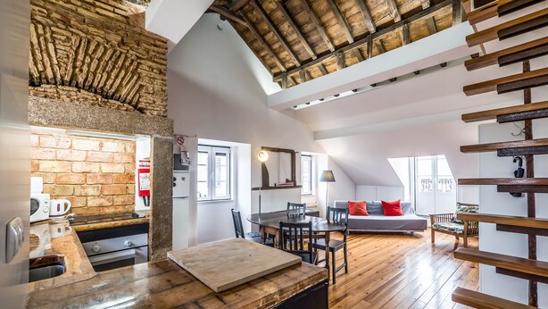 A spacious loft with exposed wooden beams, a brick wall, and a wooden dining table. - Alfama, charming attic Terrace with river view - Lisboa vida boa 1  (Lisboa)
