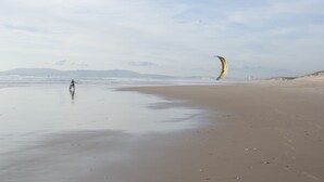 A beach with a person kite surfing, a sandy shore, and distant mountains. - Alfama, charming attic Terrace with river view - Lisboa vida boa 1  (Lisboa)