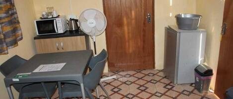 Habitación compacta con kitchenette, una mesa de comedor con sillas, un ventilador, microondas, refrigerador pequeño y un cesto de basura.