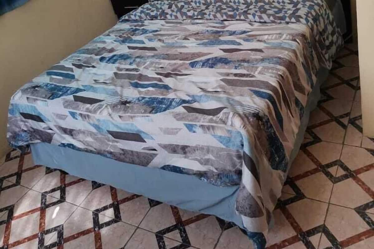 A bed with a patterned bedspread, a nightstand with a lamp, and a window with curtains.