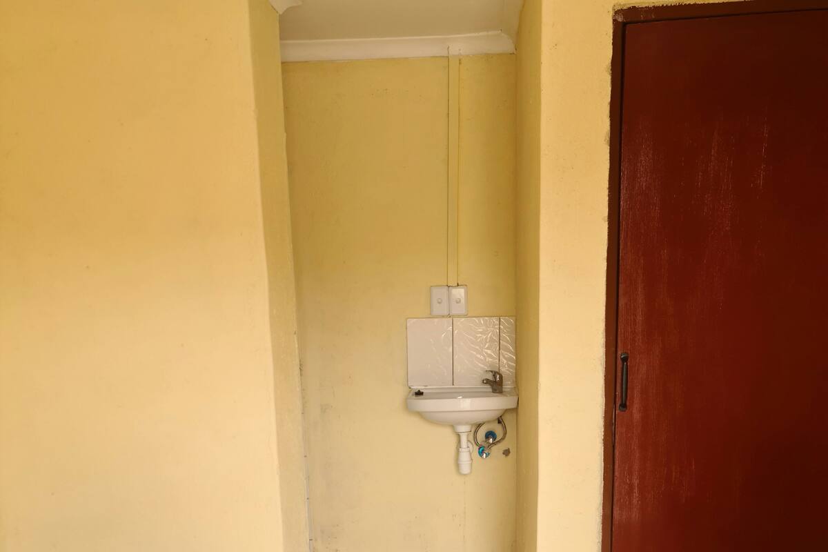 A small, narrow room with a bed, a white sink, and a heater.