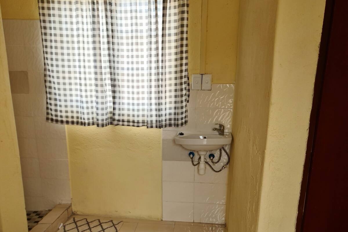 A small, yellow-walled bathroom with a checkered curtain, a sink, and a plastic bucket.