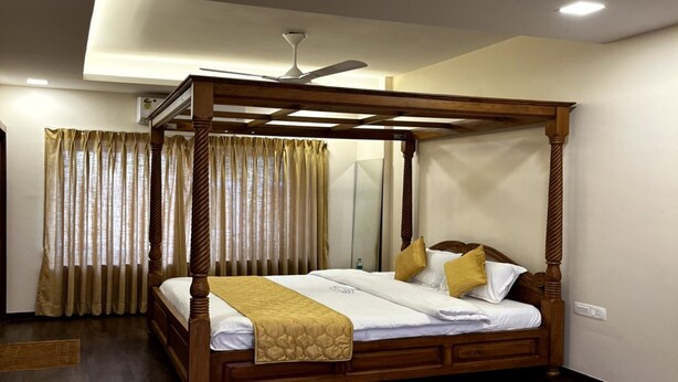 A four-poster bed with a wooden frame and a canopy, a ceiling fan, and a large window with curtains.