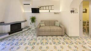 A living room with a beige sofa, a fireplace, a TV mounted on the wall, and a patterned floor.