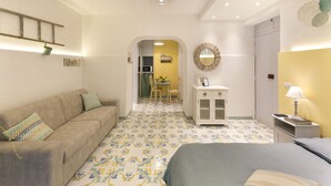 A hotel room with a sofa, a bed, a desk with a lamp, and a mirror on the wall.