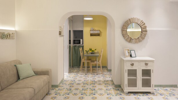 A living room with a sofa, a dining table with chairs, a small cabinet, and a mirror on the wall.