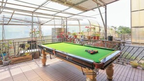 A pool table in a covered outdoor area with potted plants and a metal railing. - Boxi Haiyun Hot Spring Holiday Villa (Huizhou)
