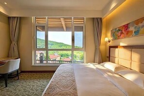 A hotel room with a large window, a bed, a desk, and a chair.