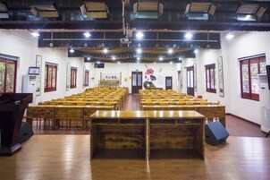Un salón amplio con filas de mesas y sillas de madera, un escenario en la parte delantera y decoraciones chinas tradicionales.