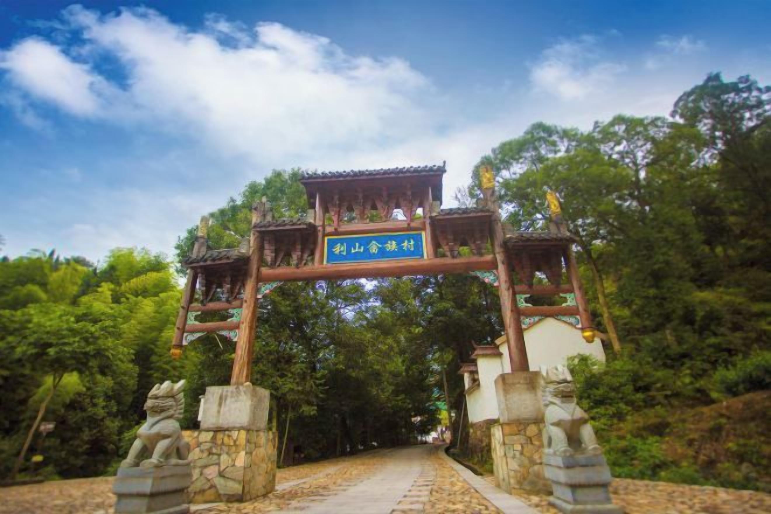 A traditional wooden gate with a sign, leading to a pathway surrounded by trees.
