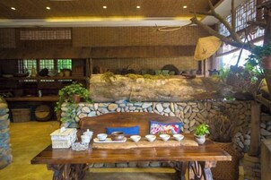 Un interior rústico con pared de piedra, una mesa de madera y varios objetos como cuencos y plantas.