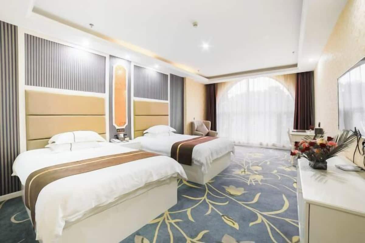 Habitació d'hotel amb dos llits, una taula de nit amb un ram de flors i una finestra gran amb cortines.