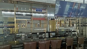 A bar area with multiple shelves of bottles, a television screen, and leather bar stools. - Nuoya Business Center Hotel (Jinggangshan City)