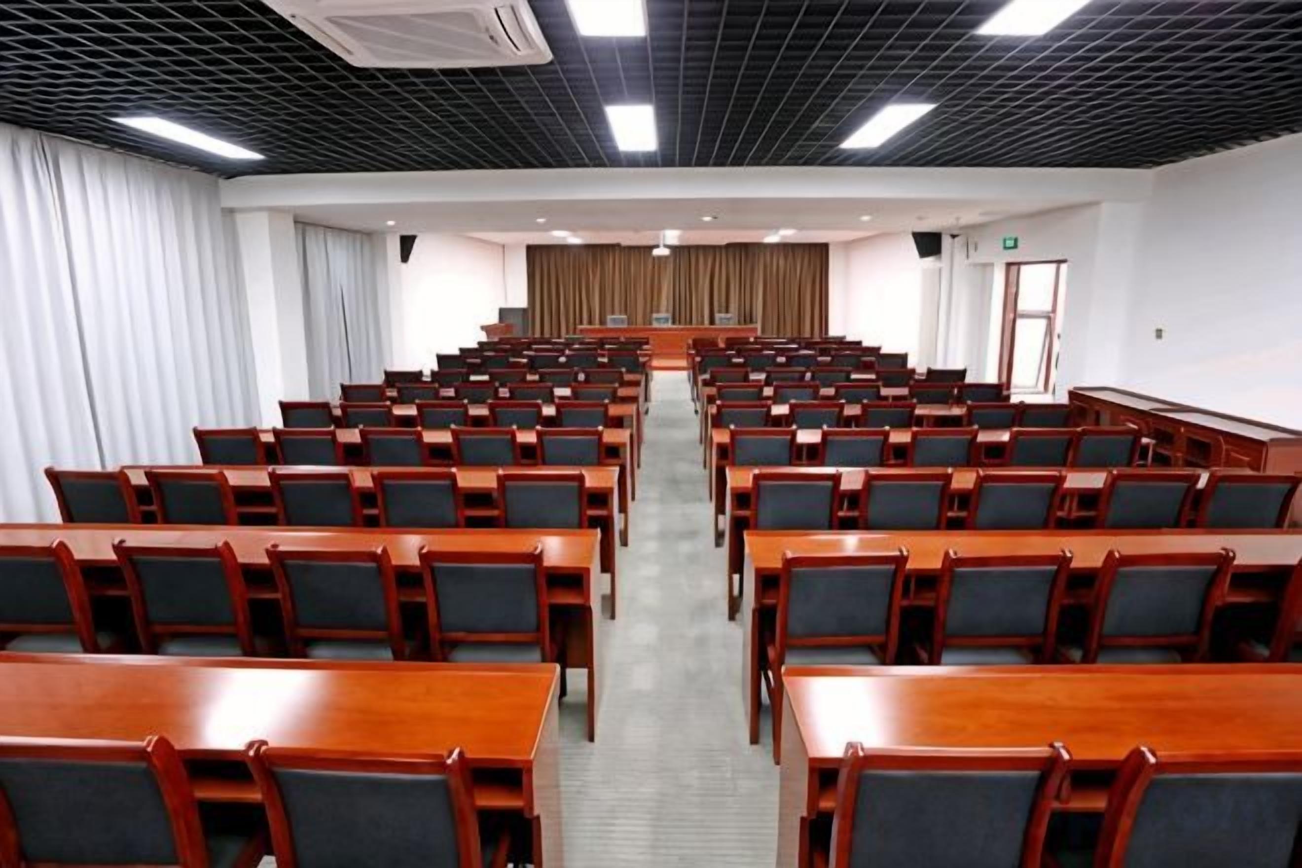 A conference room with rows of wooden tables and chairs, a podium at the front, and a curtain backdrop.