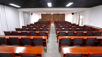 A conference room with rows of wooden tables and chairs, a podium at the front, and a curtain backdrop.