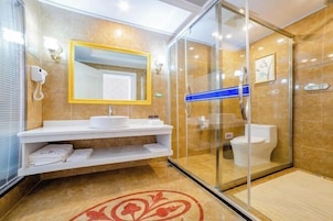 Un baño moderno con cabina de ducha de vidrio, un lavamanos blanco y un espejo con marco amarillo, y un piso de baldosas color beige.
