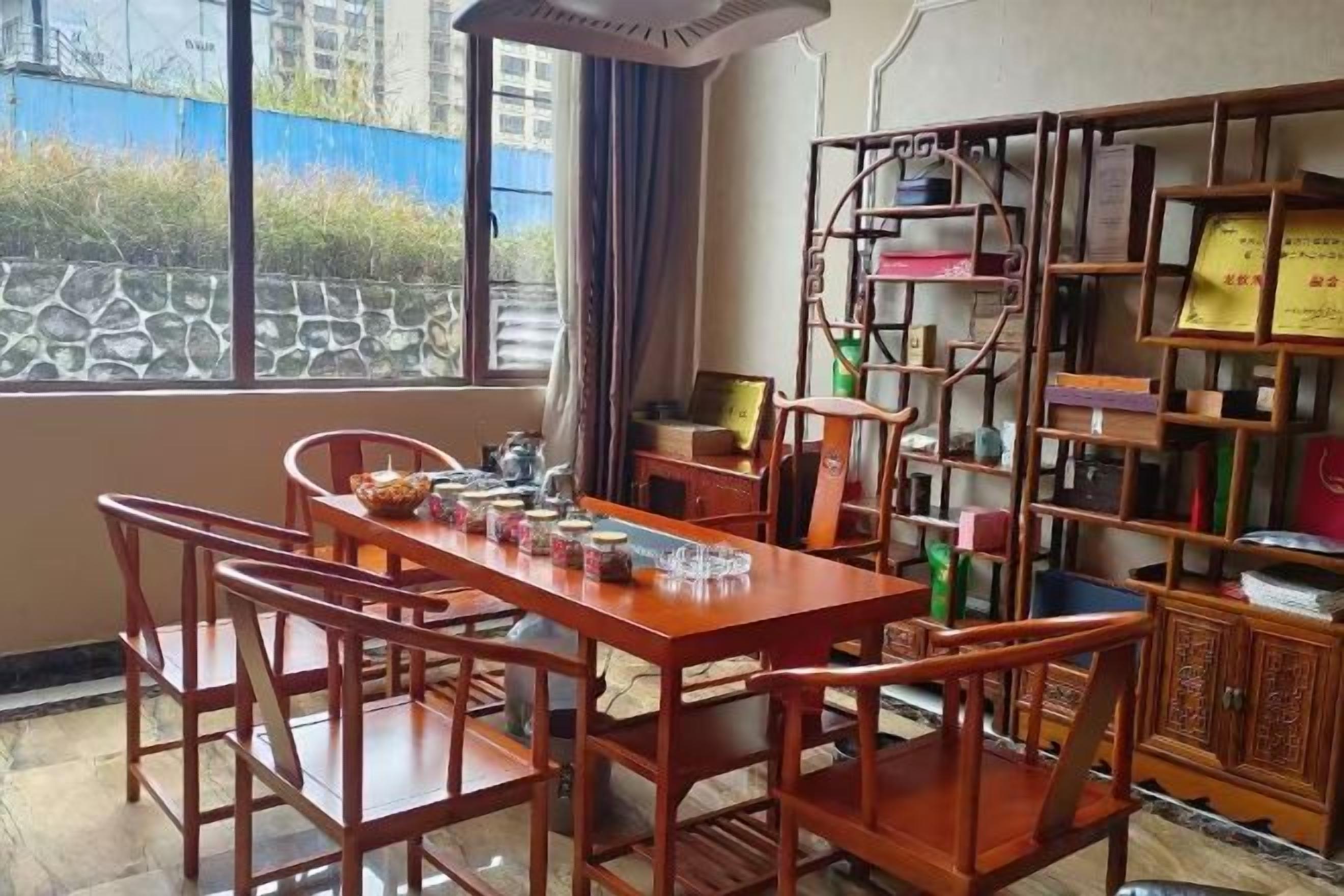 A dining area with a wooden table and chairs, a bookshelf, and a view through a window.