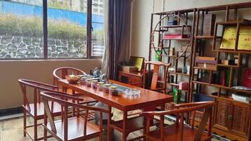 A dining area with a wooden table and chairs, a bookshelf, and a view through a window.