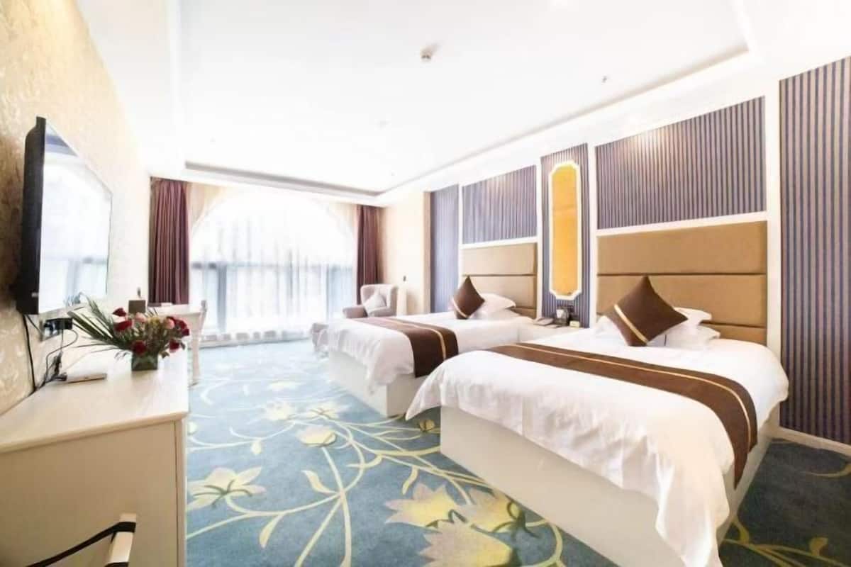 Habitació d'hotel amb dos llits, un escriptori i una finestra gran.