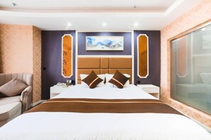 A hotel room with a large bed, a nightstand, a sofa, and a large window.