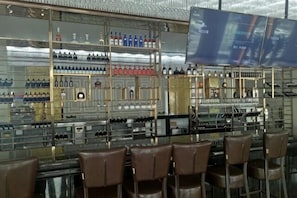 Una zona de bar con múltiples estantes llenos de botellas y vasos, y varias sillas marrones.
