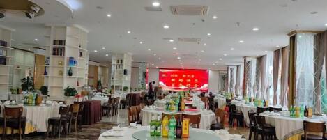 A banquet hall with round tables, chairs, and a stage with a red backdrop.