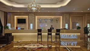 A hotel reception area with a modern design, featuring a reception desk, three chairs, a chandelier, and a wall-mounted TV. - Nuoya Business Center Hotel (Jinggangshan City)