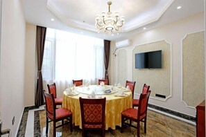 A dining area with a round table, red upholstered chairs, a chandelier, and a flat-screen TV mounted on the wall. - Nuoya Business Center Hotel (Jinggangshan City)