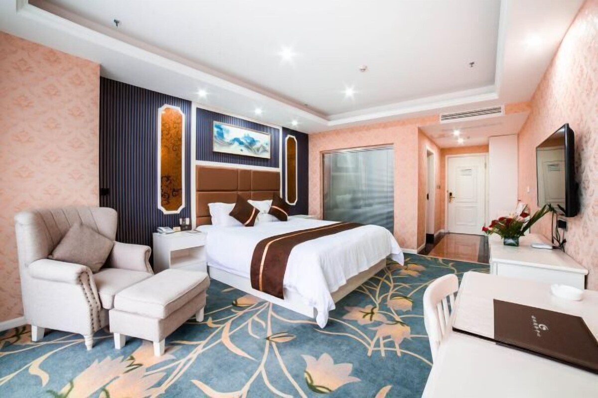 Ein Hotelzimmer mit Bett, Schreibtisch, Sessel, Sofa und Fernseher.