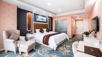 A hotel room with a bed, a desk, a chair, a sofa, and a TV.