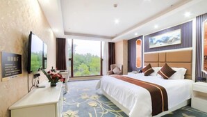 A hotel room with a large bed, a desk, a TV, and a view of greenery outside. - Nuoya Business Center Hotel (Jinggangshan City)