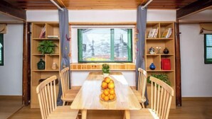 Une table à manger en bois, entourée de chaises, une fenêtre donnant sur un paysage enneigé et des étagères en bois remplies de divers objets.