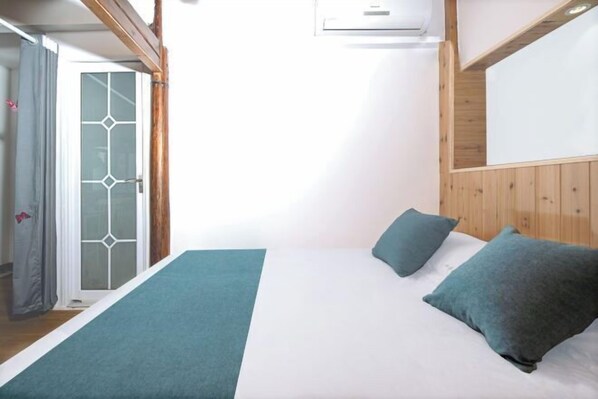 A bedroom with a bed, pillows, a window, and an air conditioning unit.