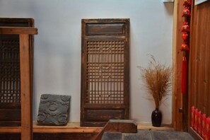 A traditional wooden door with intricate carvings, a stone slab with a circular pattern, and a vase with dried plants. - Alley Time Inn (Wuyuan)