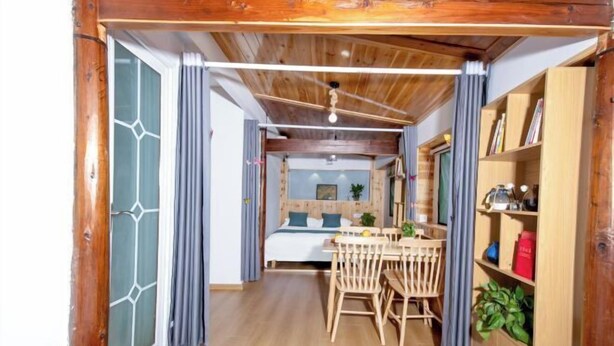 Une pièce chaleureuse avec un plafond en bois, un lit doté d’une tête de lit bleue, une table à manger en bois avec des chaises et une bibliothèque.